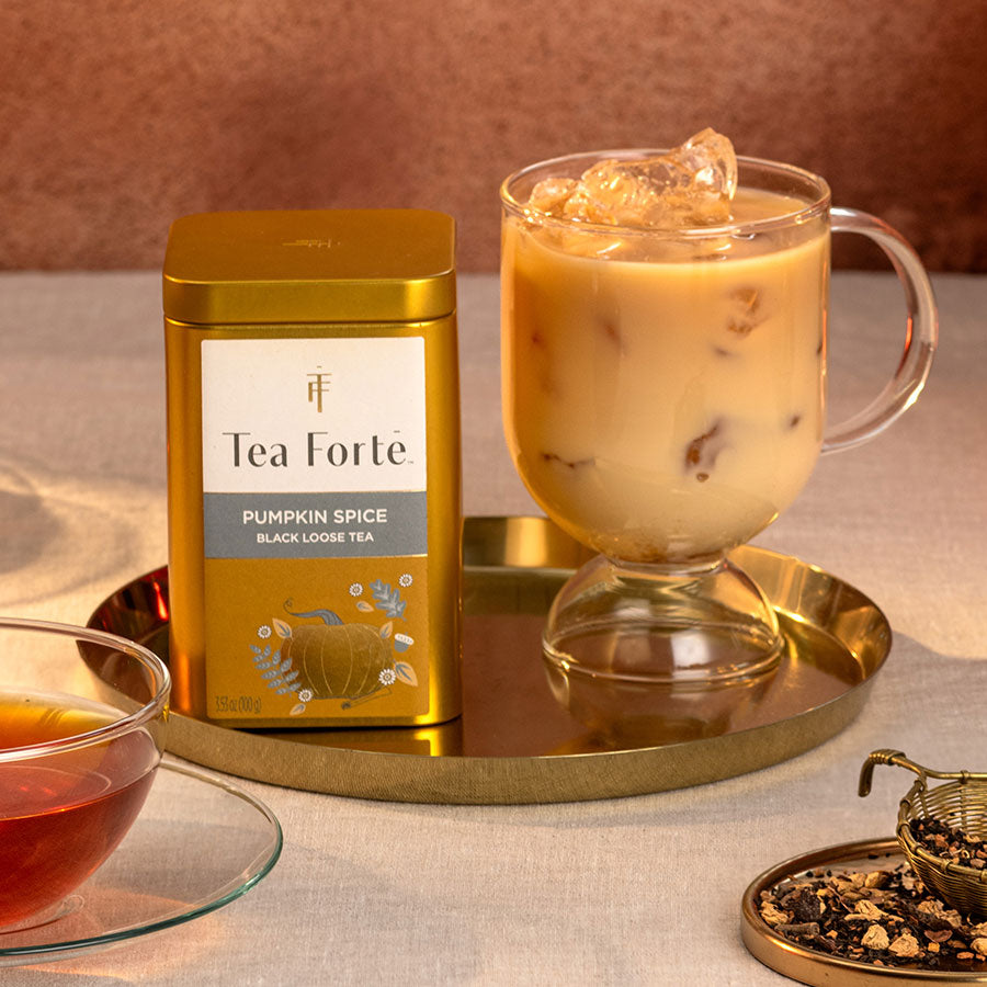 Pumpkin Spice Loose Lea Canister with a glass of iced pumpkin spice tea on a gold tray with loose tea leafs on a plate nearby