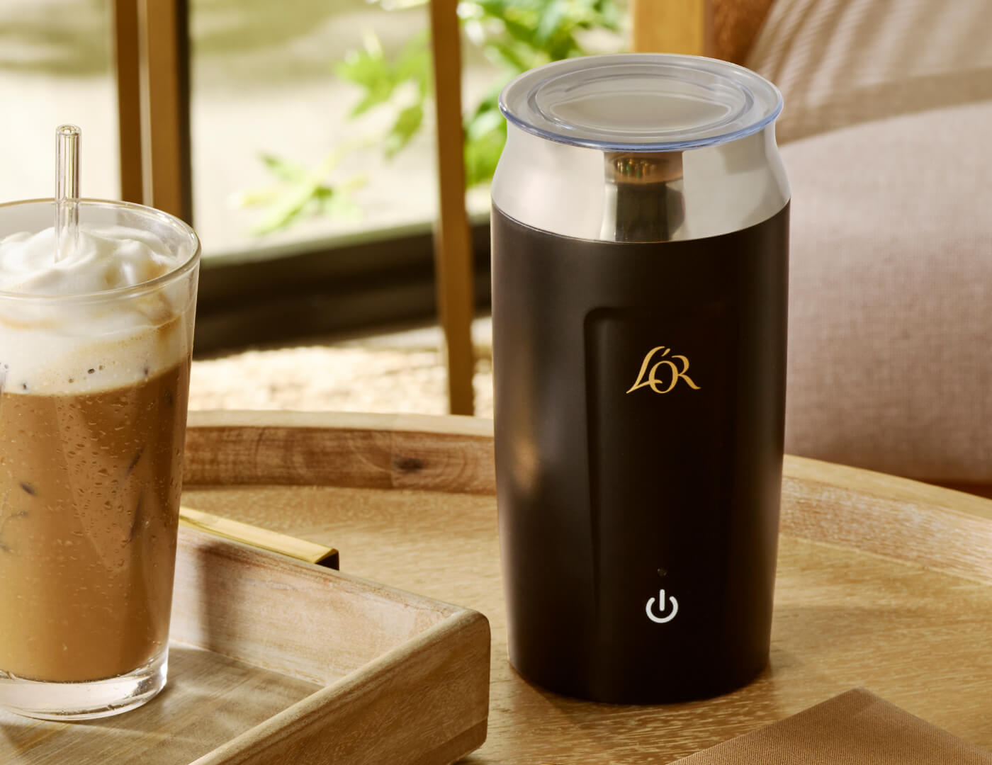 Black milk frother with a glass of iced tea latte on a wooden table.