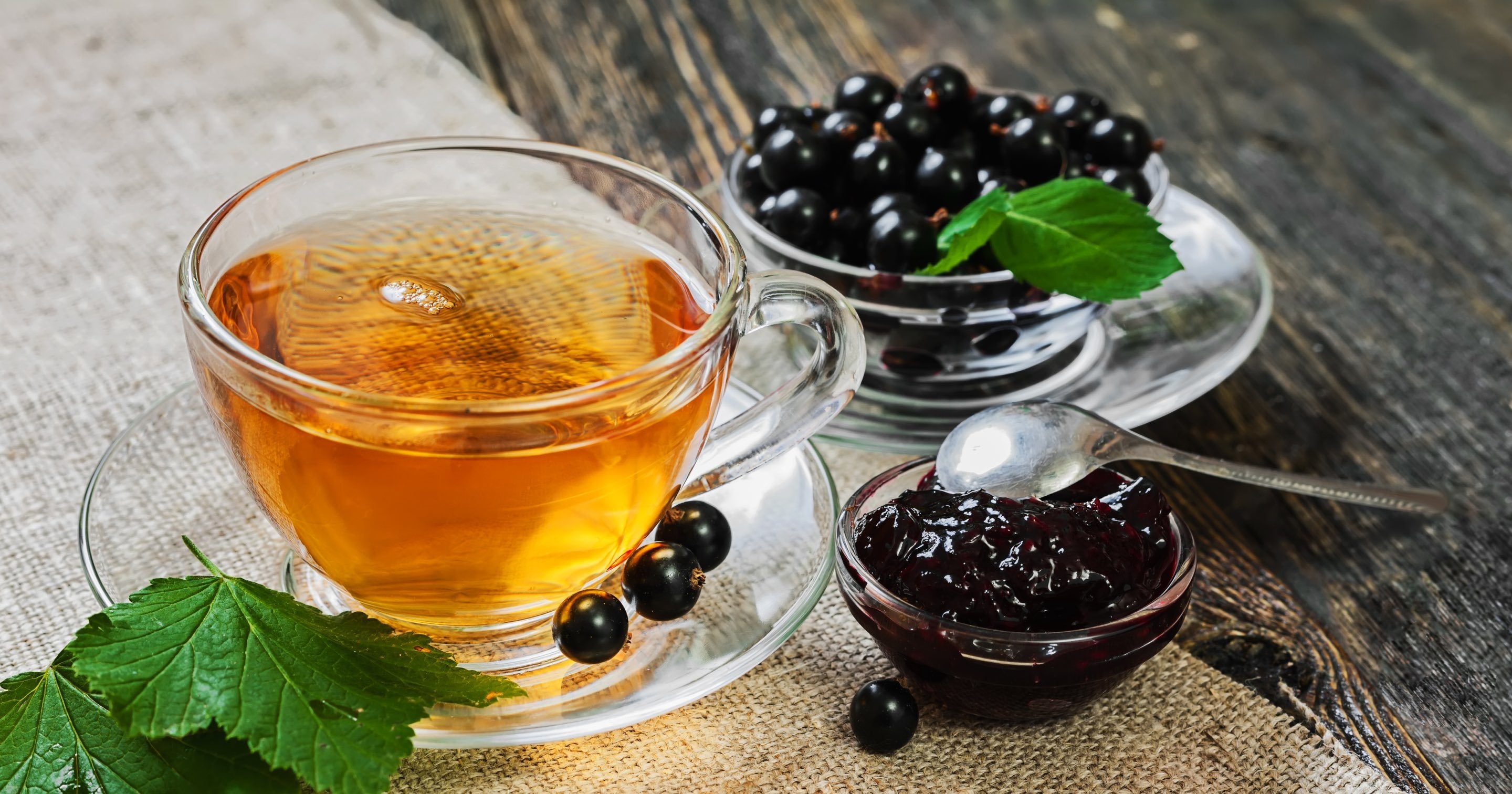 A glass cup of black currant tea with black currants and jam