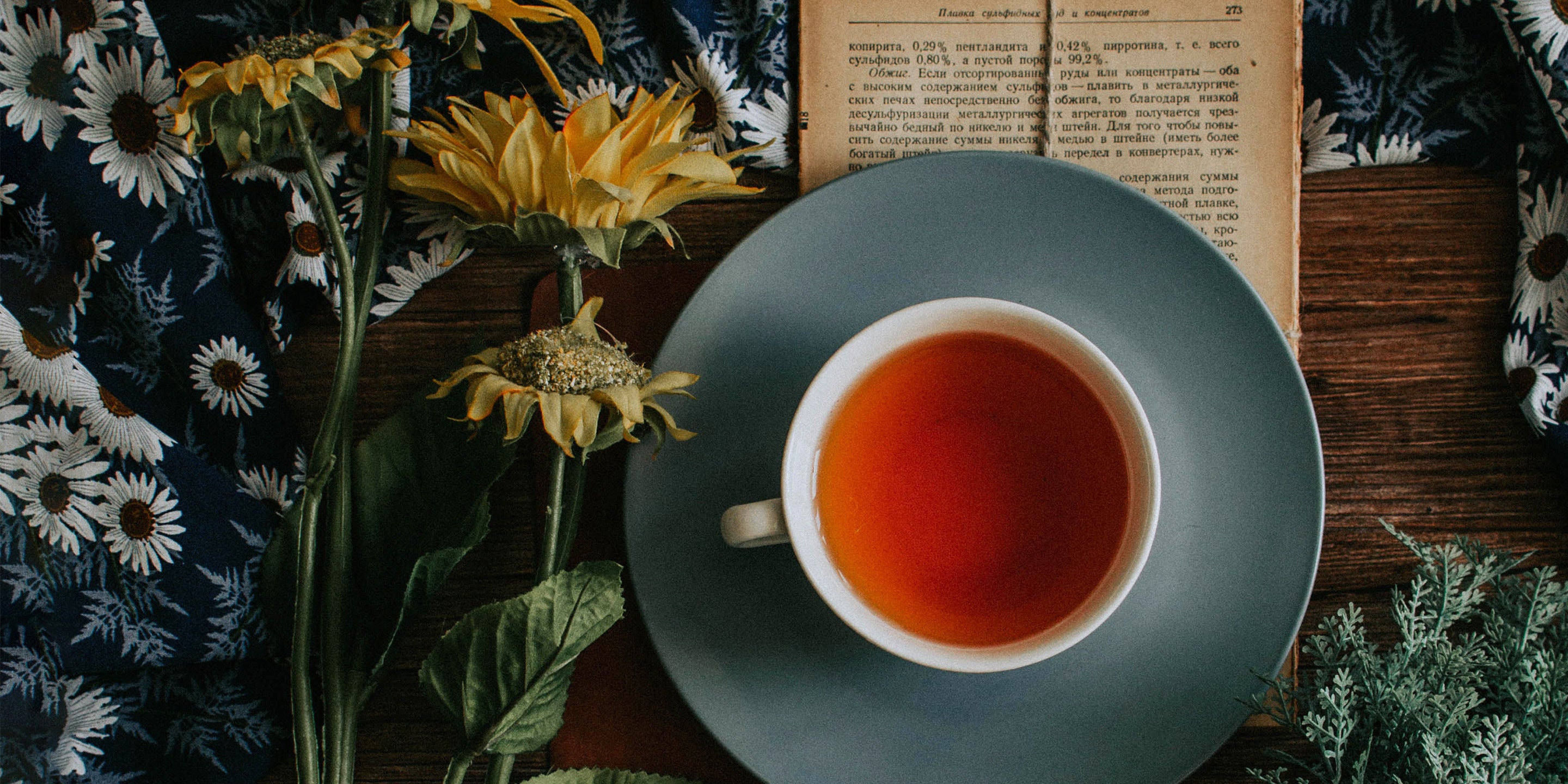 A ceramic cup and saucer of earl grey tea with flowers seen from above