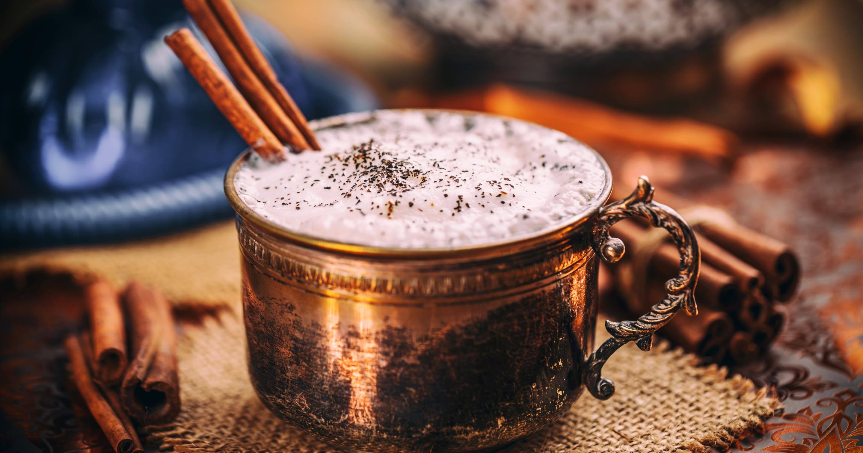 Chai tea latte in a copper mug with a cinnamon stick and a milky, frothy top