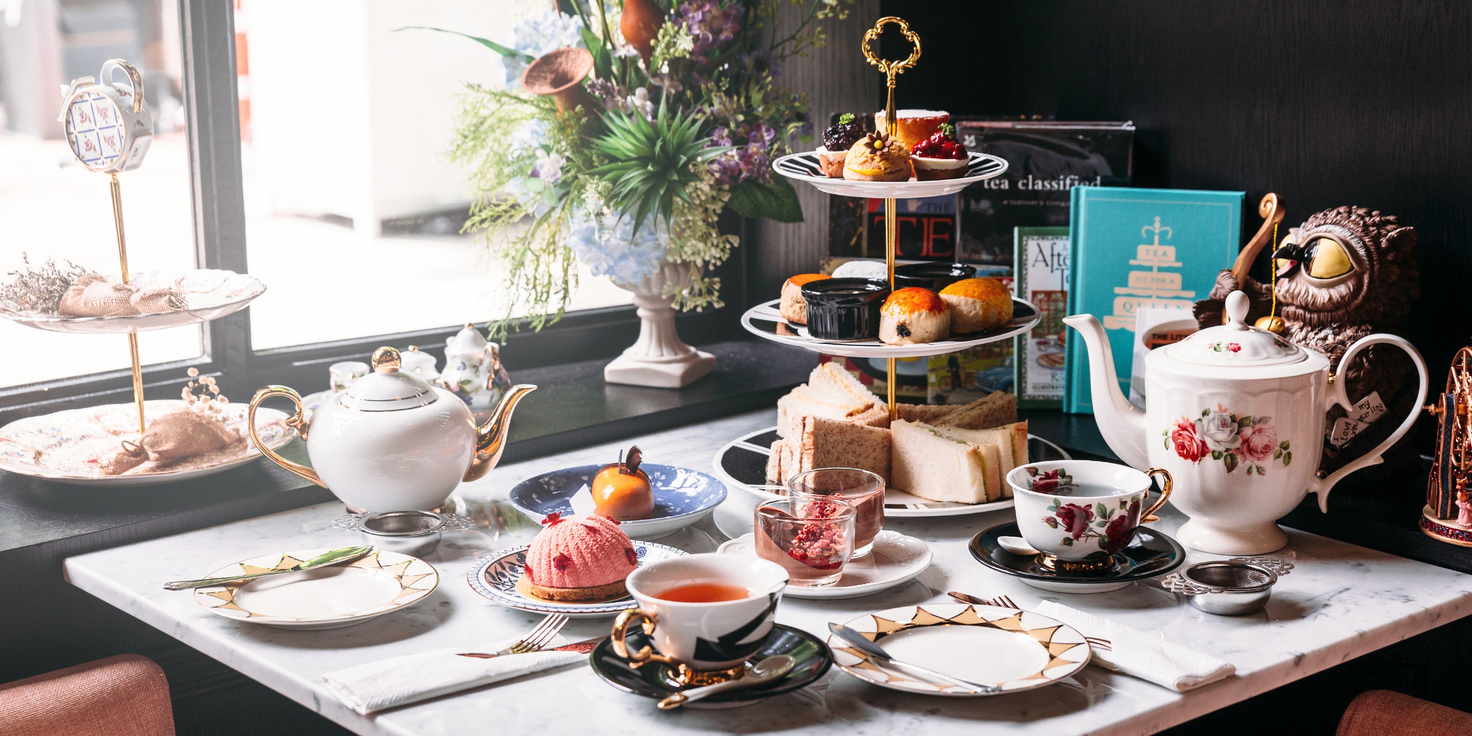 A windowside table in a Bed & Breakfast filled with small snack sandwiches, teapots, teacups and fruit