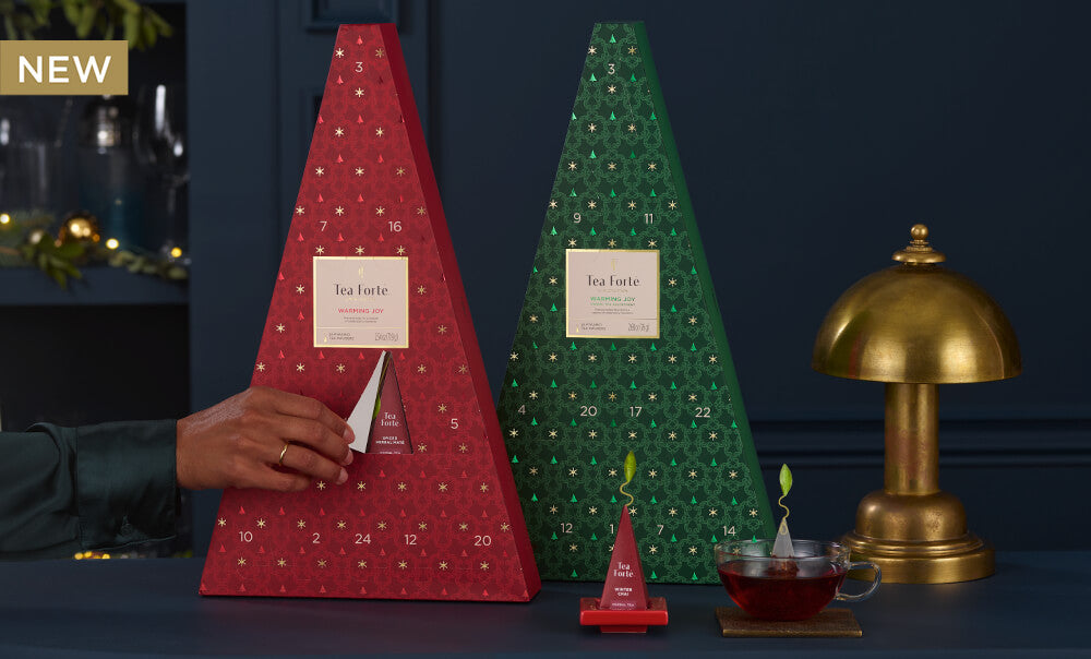 Red and green tea tree-shaped advent calendars with a hand opening one, on a dark background.