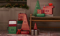Warming Joy items in red and green arranged on a bench with reddish walls and Christmas pine trimmings, with gifts and ribbons