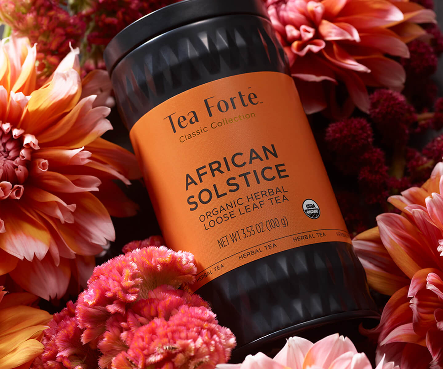 African Solstice loose tea canister laying on a background of of red & pink flowers