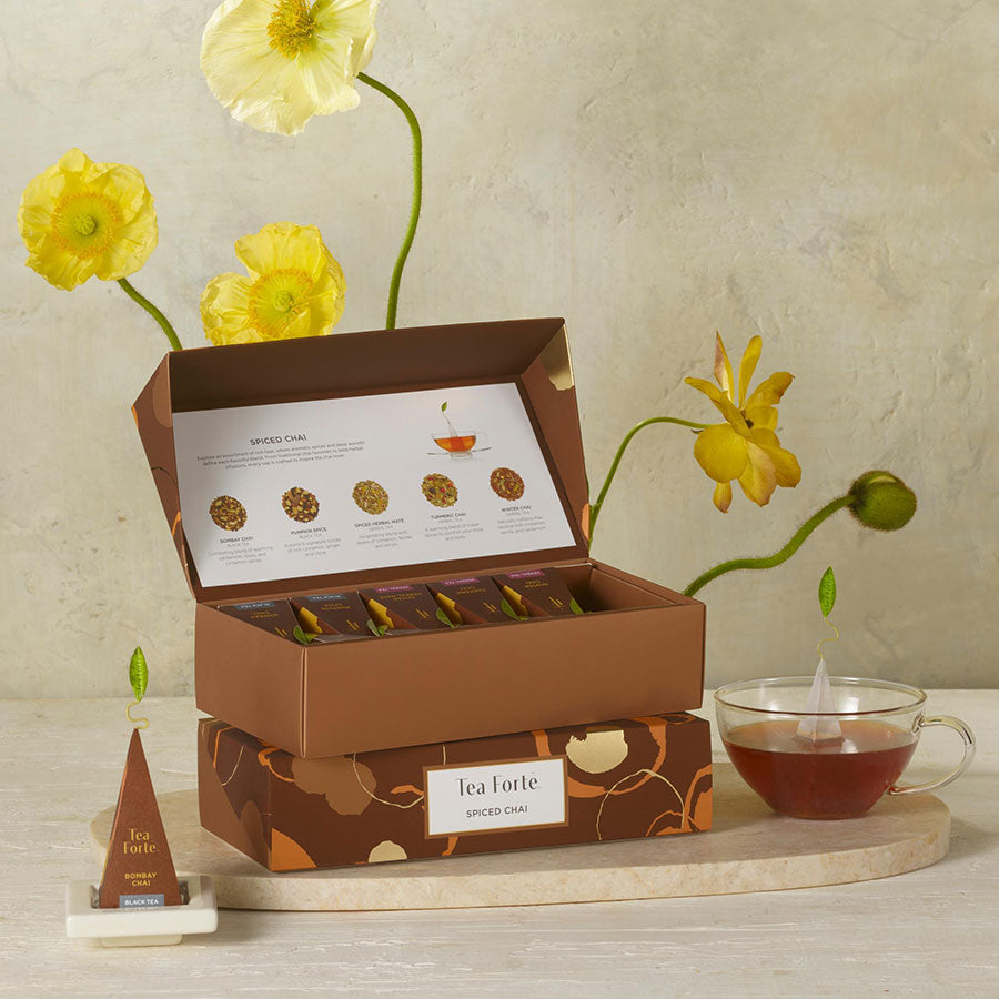 Two Spiced Chai Petite Presentation Boxes stacked on top of one another with a glass cup of tea and yellow flowers