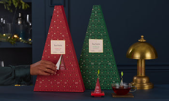 Two Warming Joy Advent Calendars on a desk, with a hand opening one of the doors, exposing a tea infuser inside