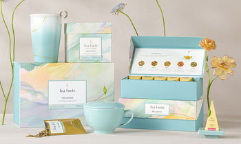 Wellbeing Collection of boxes including one open with tea menu displayed and light blue accessories to match with light blue flowers on a pale background.