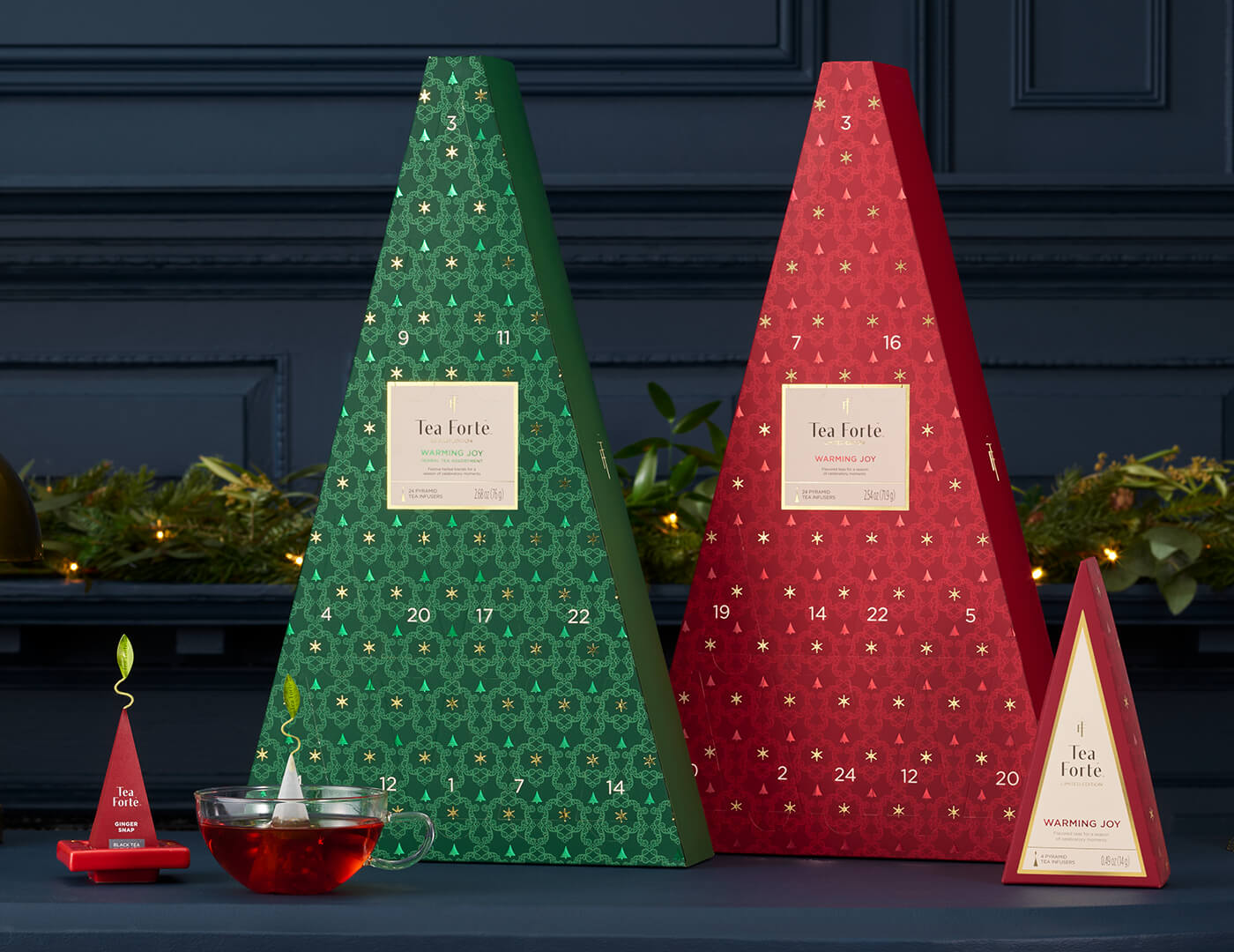 Two triangular Advent Tea Calendars, one red, one green, with numbered doors with a cup of tea and other items in foreground