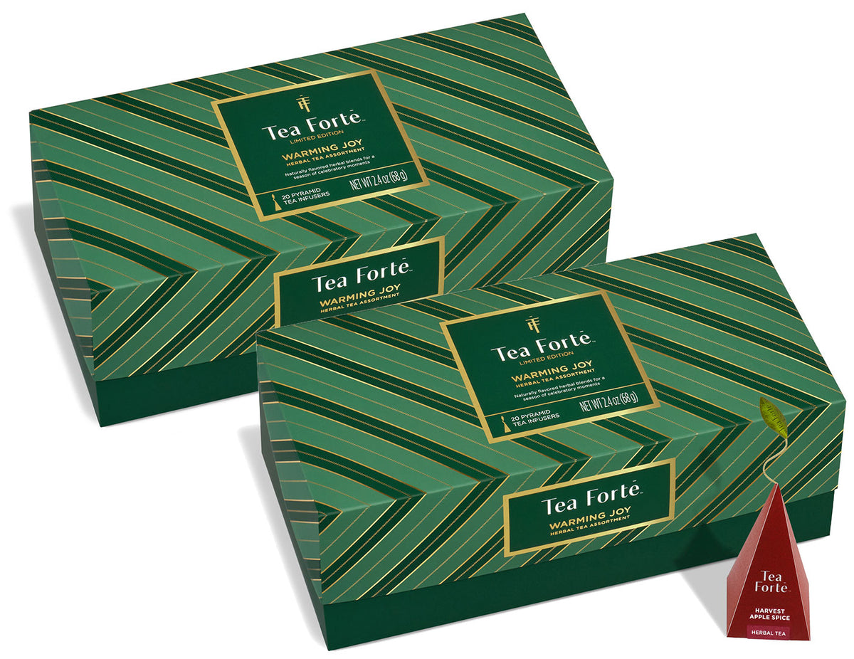 Two green Tea Forté Warming Joy Herbal Tea Presentation Boxes with gold geometric stripes and a single red pyramid tea infuser shown beside them on a white background.