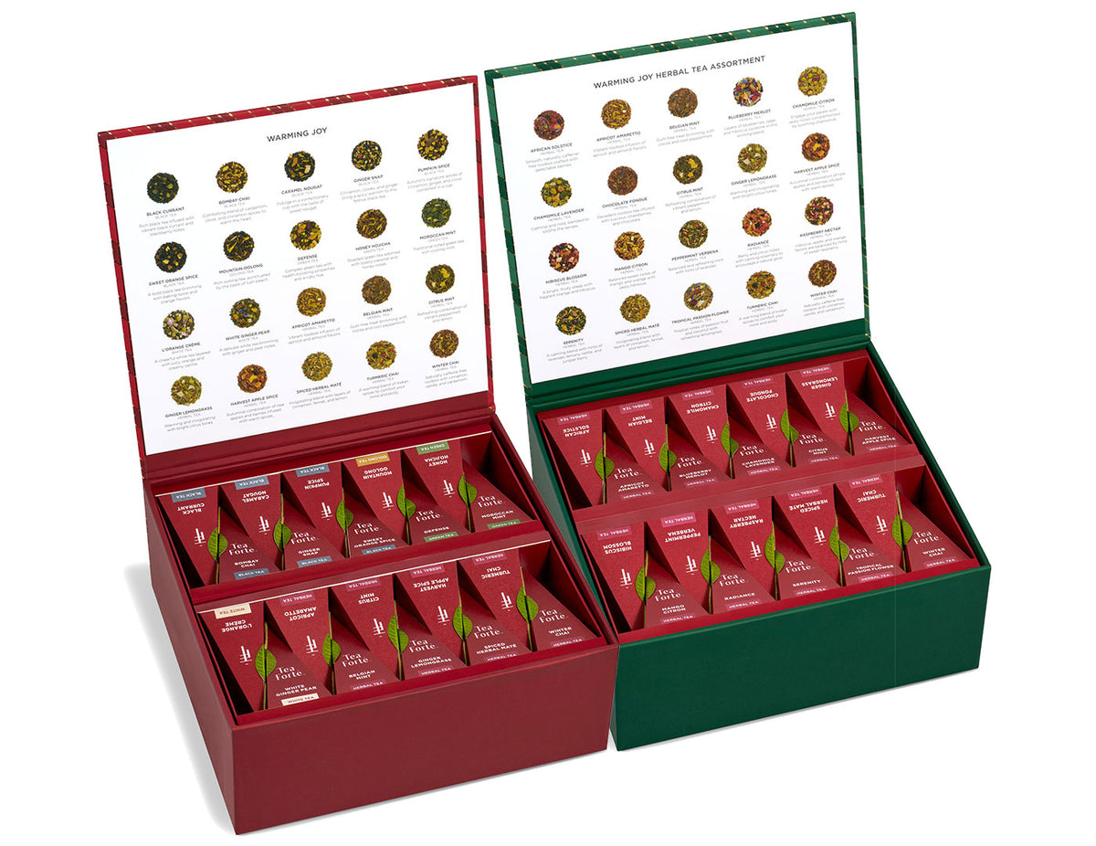 Two open Warming Joy Tea Chests displayed side by side on a white background. The left box is dark red and filled with assorted teas, and the right box is dark green and filled with herbal teas.