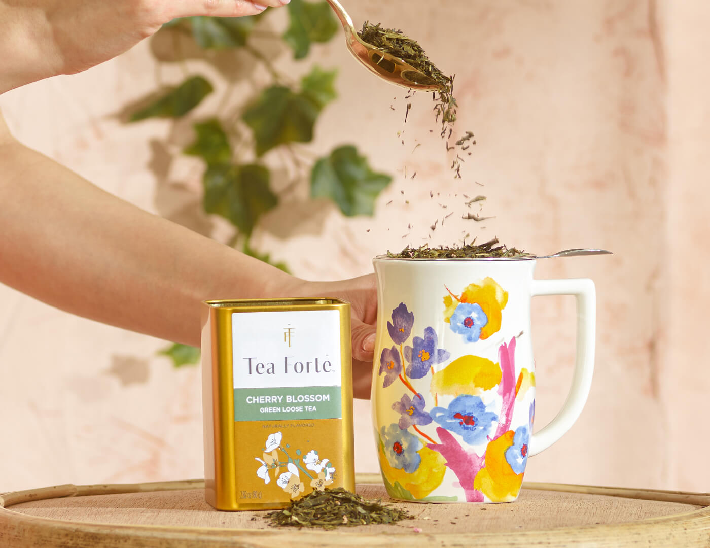 Hand holding spoon pouring Cherry Blossom loose tea leaves into a Volaré Fiore Steeping cup, and a n open Loose Tea Canister of Cherry Blossom off to the side