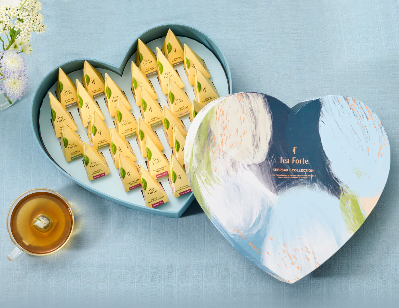 Keepsake Heart Box, Something Blue, of 26 pyramid infusers, lid open, revealing infusers, with cup of tea on light blue background