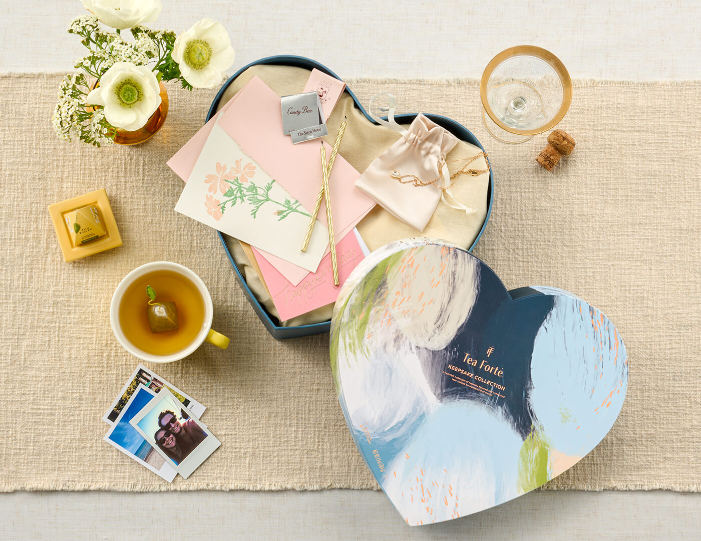 Keepsake Heart Box, Something Blue, of 26 pyramid infusers, lid open, revealing infusers, with cups of tea on a table with and birthday items