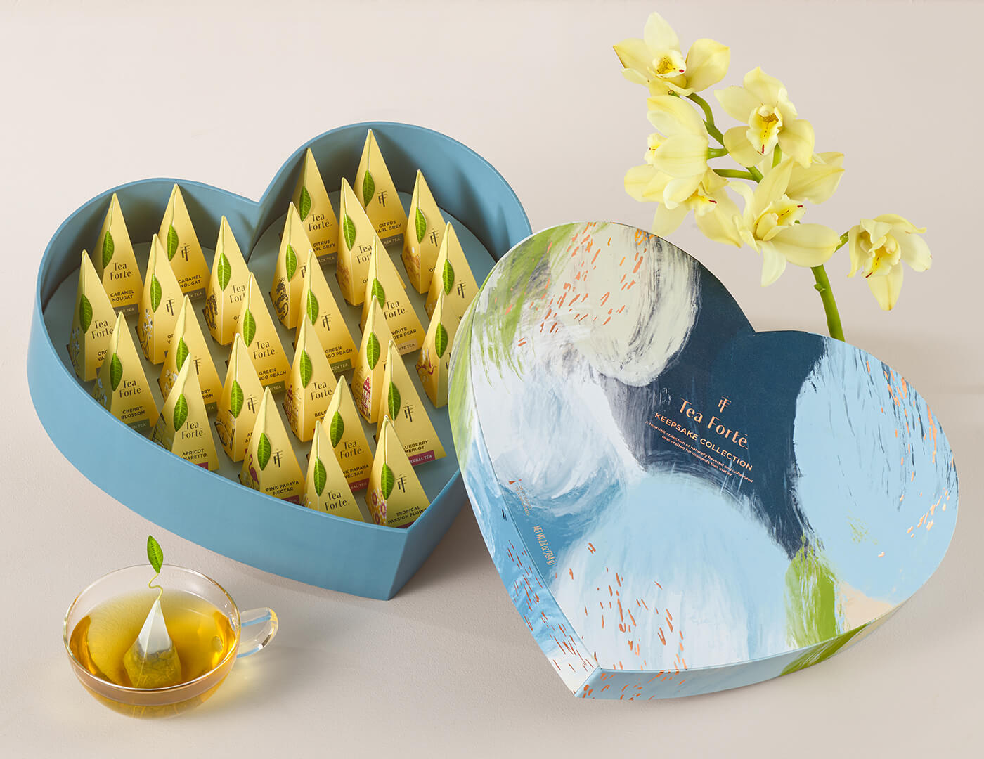 Keepsake Heart Box, Something Blue, of 26 pyramid infusers, lid open, revealing infusers, with cup of tea and flowers