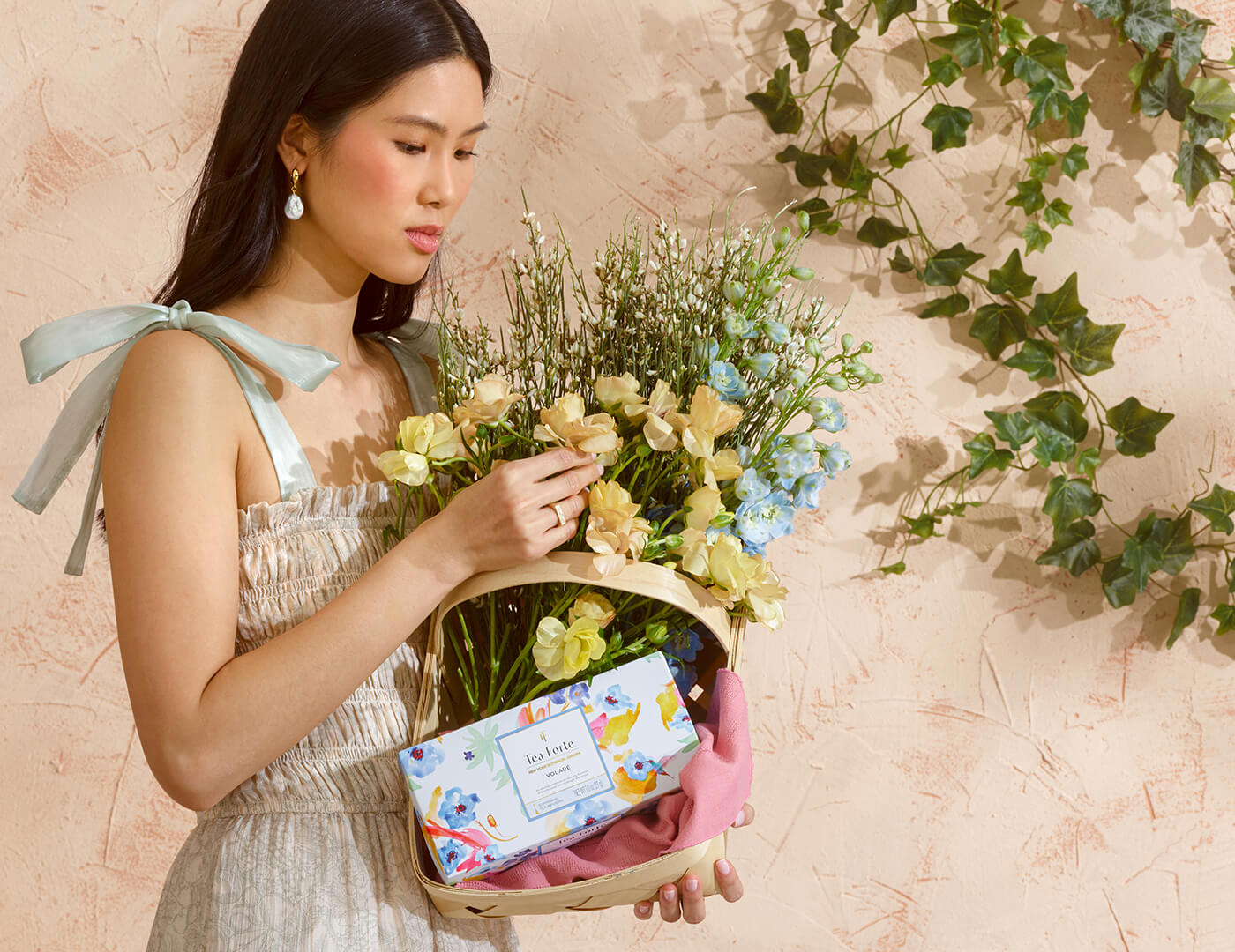 Woman holding a basket of flowers with a Volare Presentation Box inside against a beige wall with greenery.