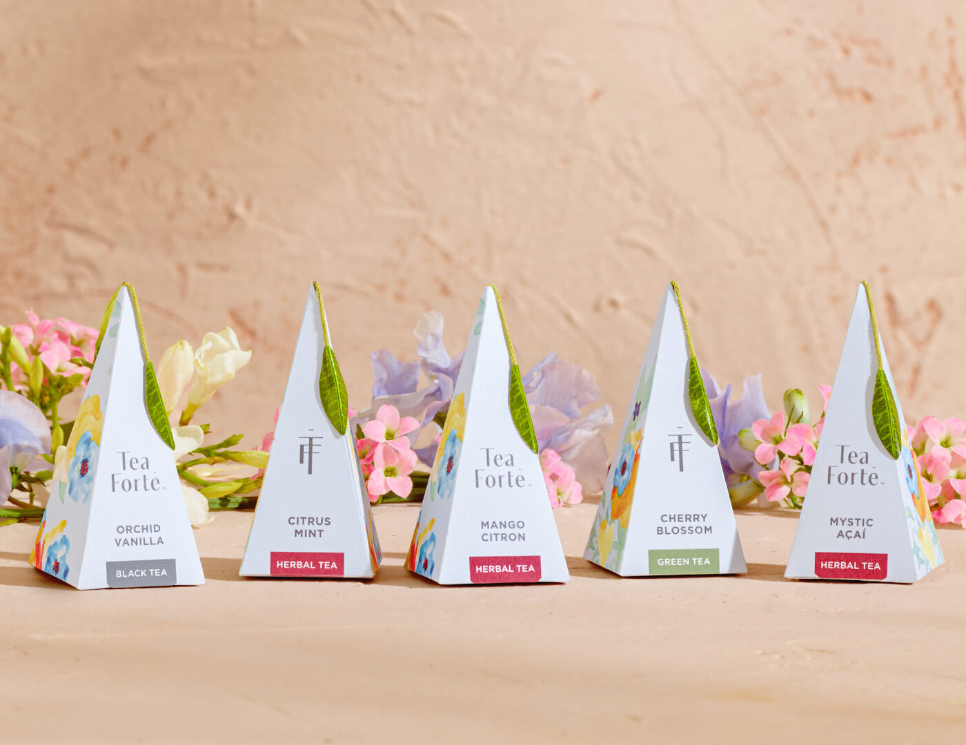 Volare pyramid tea infusers, one of each blend on a tan background with flowers