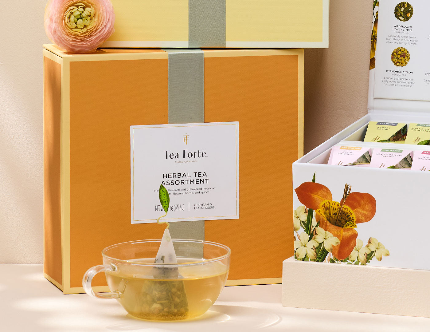 MAIN PDP | Herbal tea assortment Tea Chest with lid closed and glass of tea and pink flower amongst  other Tea Chests