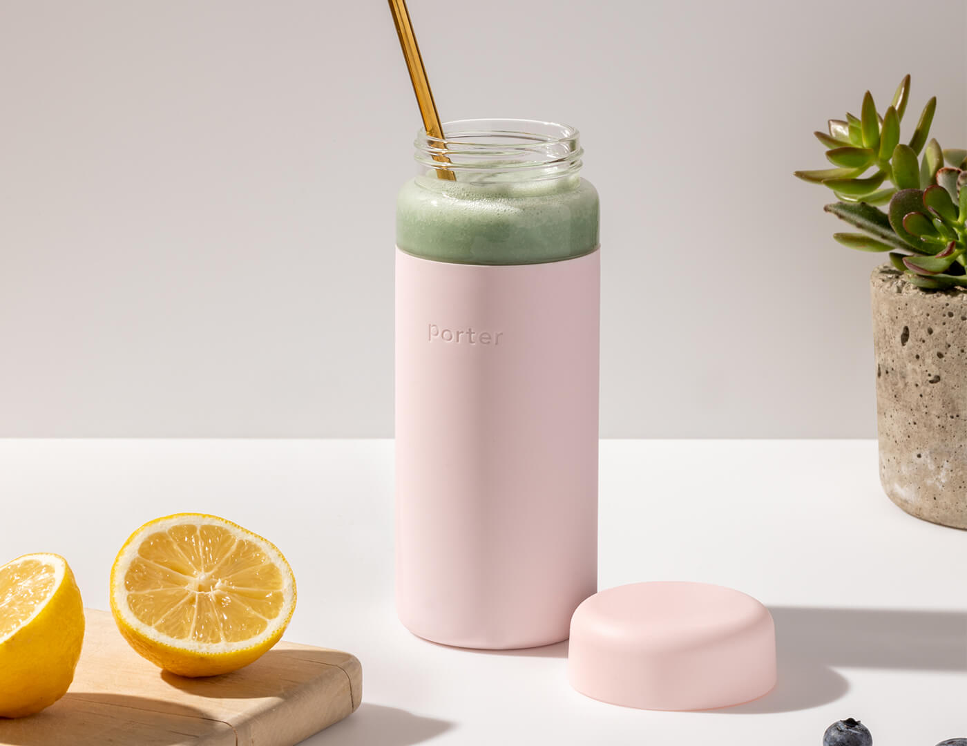 Blush Porter Water Bottle resting on table with fruit, filled with a green smoothie