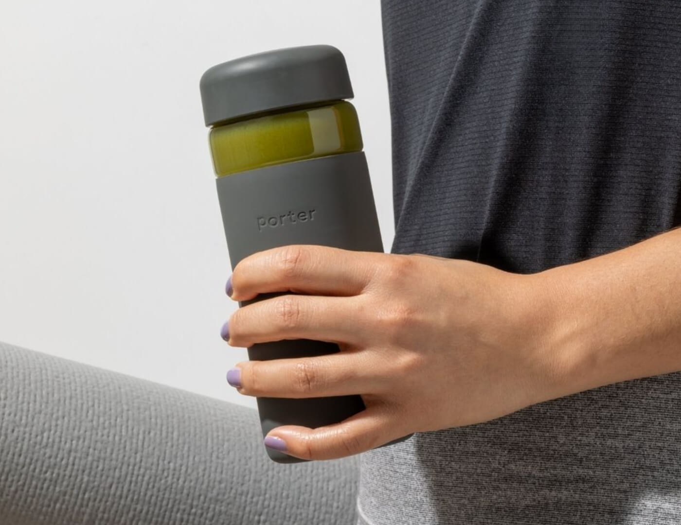 Person holding a Charcoal Porter water bottle against a light gray background, with yoga mat rolled up