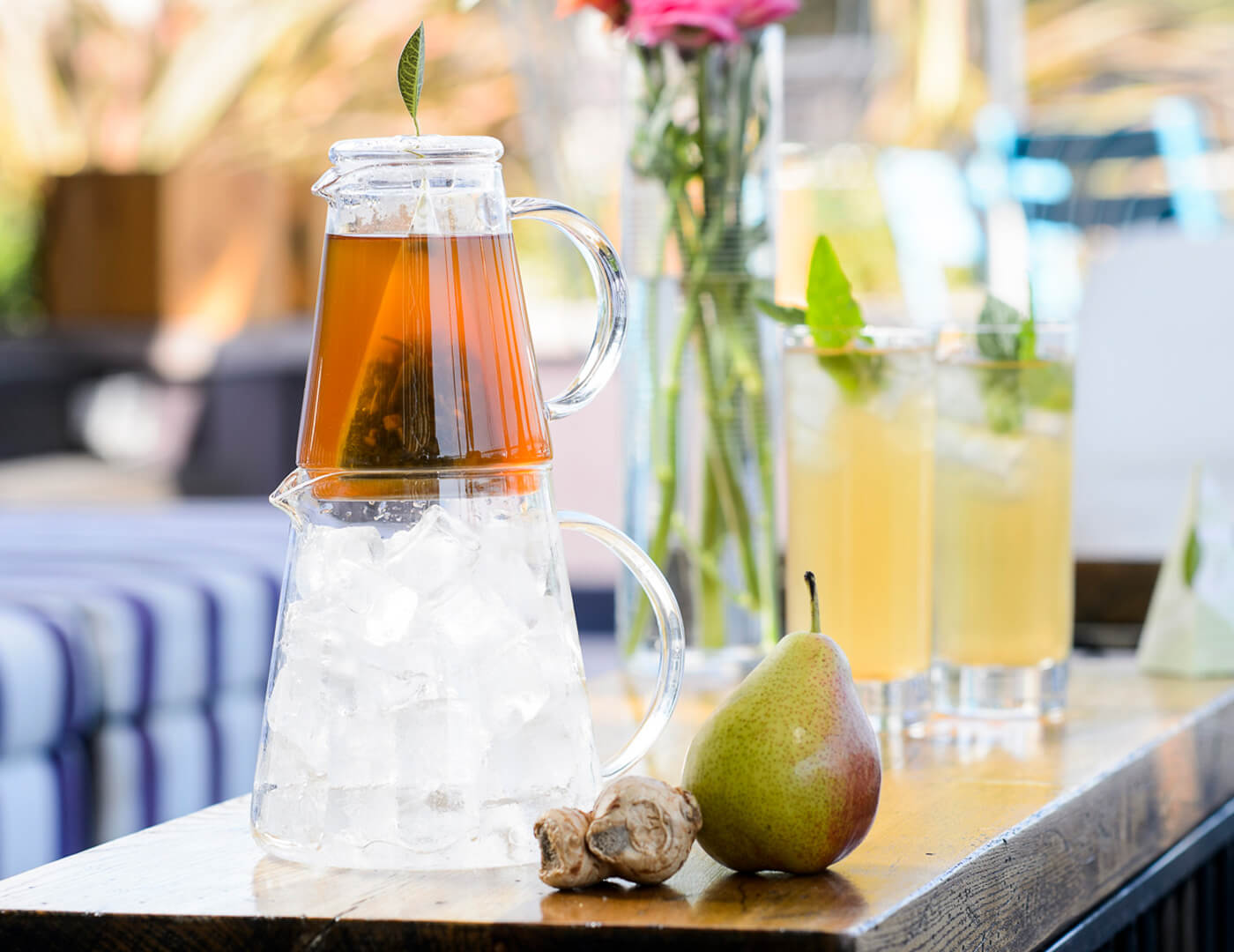 Tea Over Ice Pitcher of White Ginger Pear with a pear and ginger root on a table with glasses of iced tea