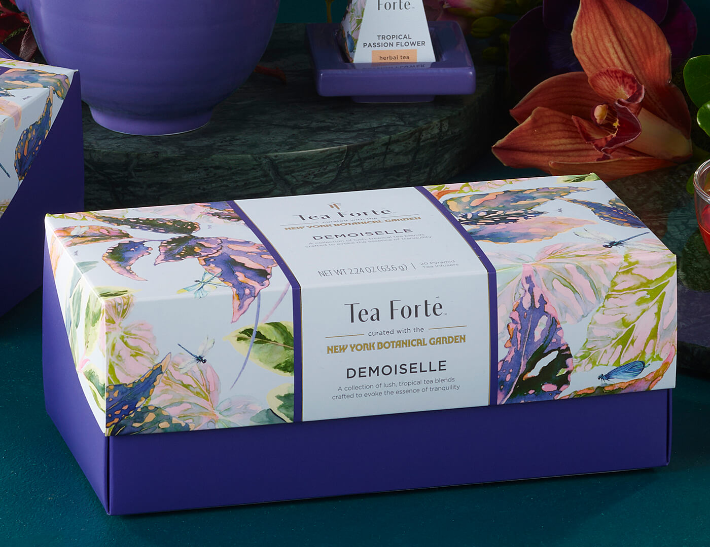 Demoiselle Presentation Box of 20 infusers, closed, amongst moss and plants and other Demoiselle items