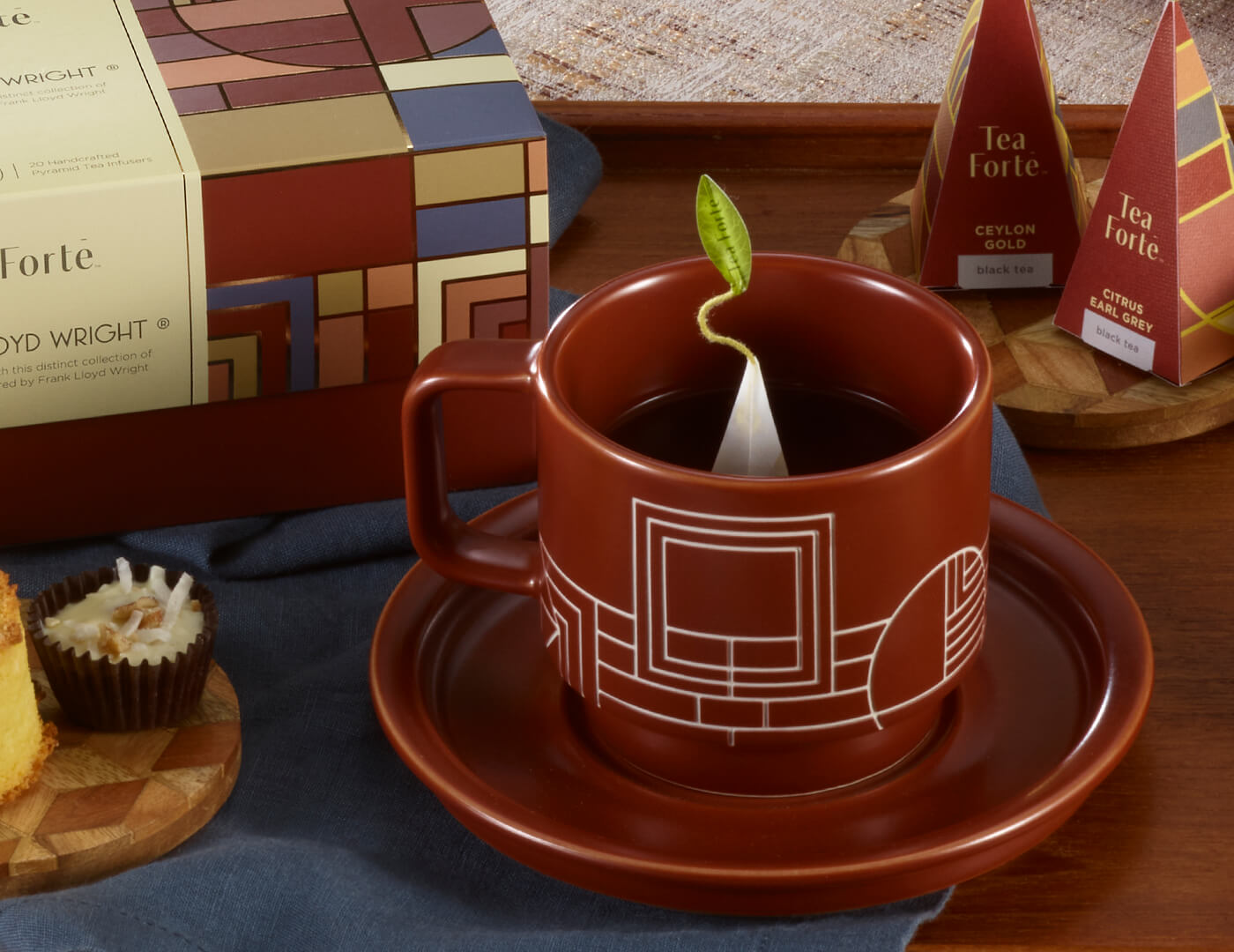 Terra stoneware teacup and saucer on a table with the Frank Lloyd Wright tea collection, desserts and pyramid tea infusers