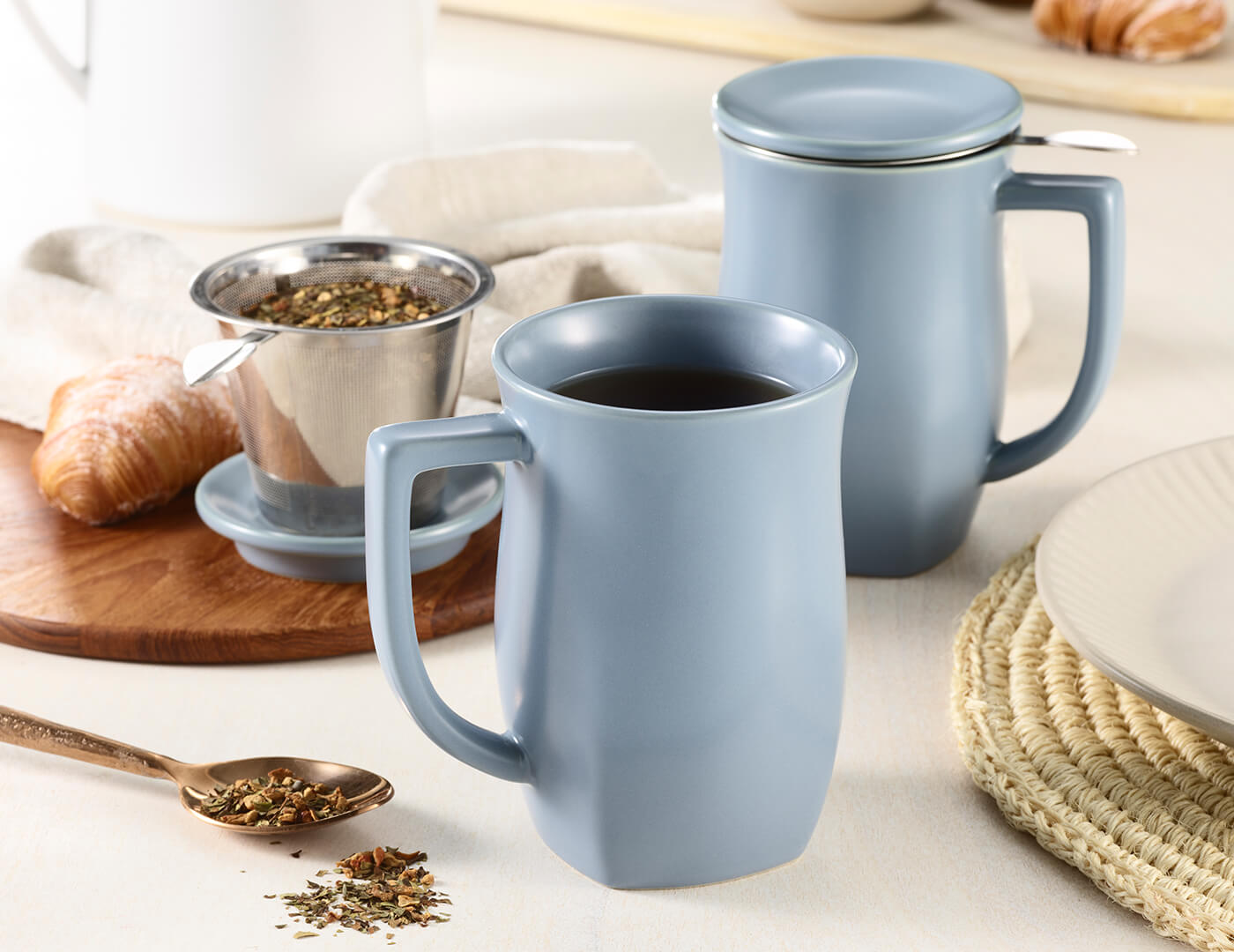 Fiore Steeping Cup and infuser in Stone Blue on a table with tea and croissants