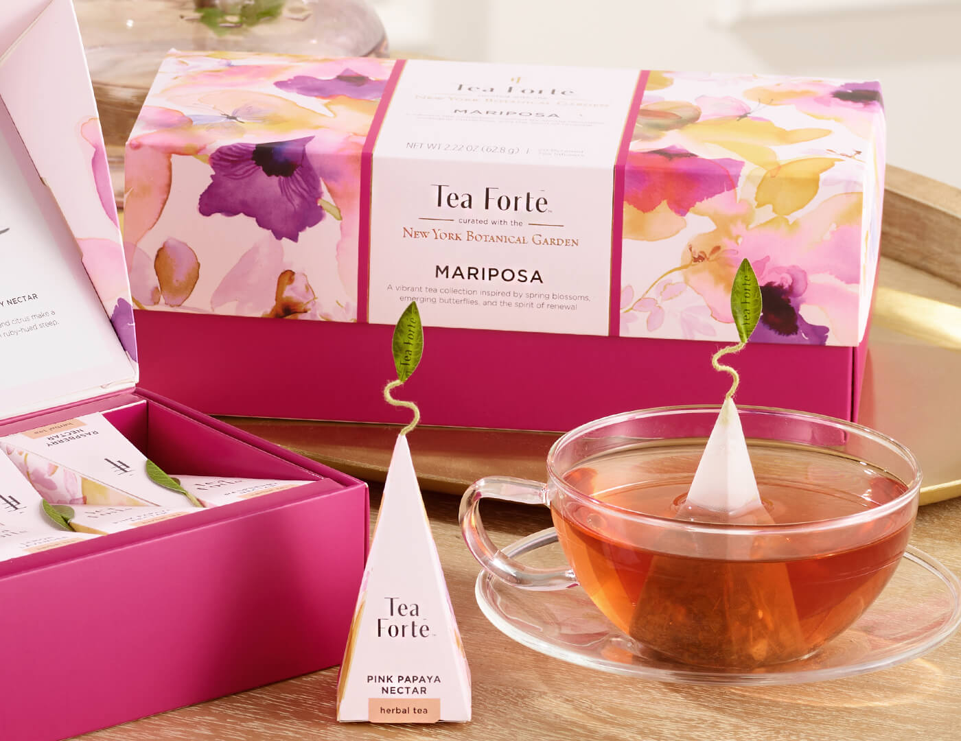 Mariposa Presentation Box of 20 pyramid tea infusers, closed box o a table with a glass cup of tea and other boxes and infusers
