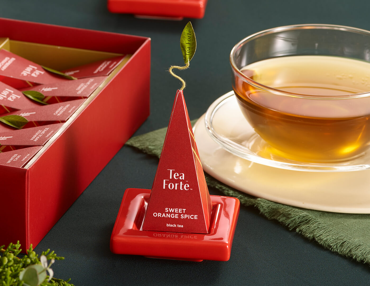 Ruby Red Tea Tray with infuser perched on top resting on festive table with cup of tea and Warming Joy Petite Box open