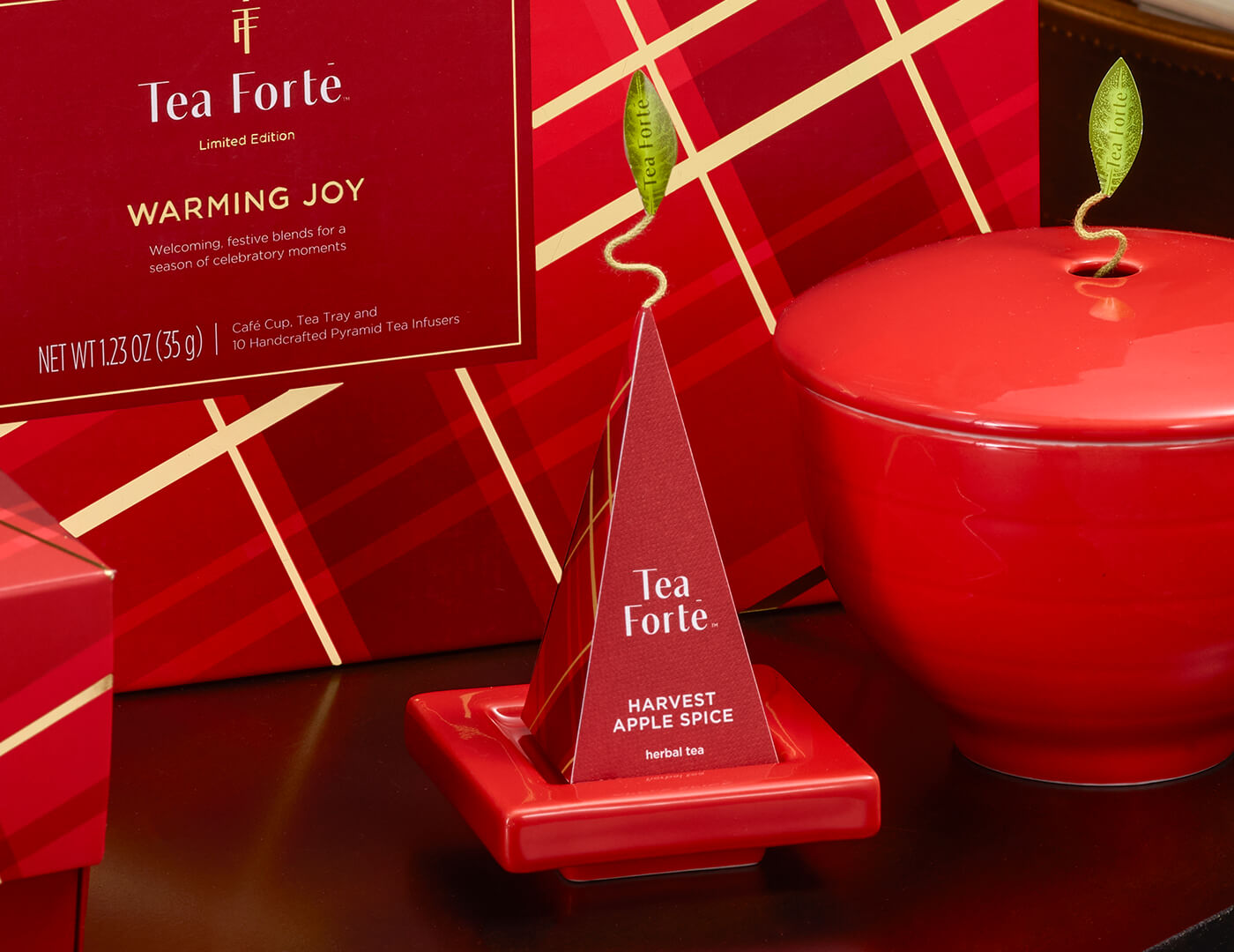 Ruby Red Tea Tray with infuser perched on top resting on festive table with a Ruby Red Café Cup and Warming Joy Gift Set
