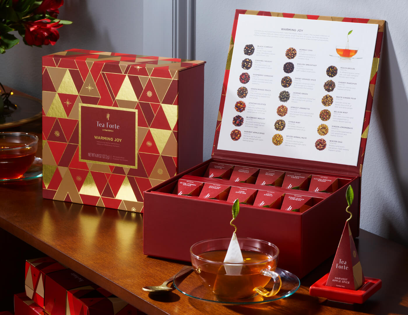 Tea Chest Warming Joy, open and closed on a wooden counter with a glass teacup, infusers