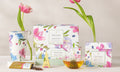 Herbal Retreat tea assortment in various boxes on table with a pyramid tea infuser,  teacups, pouch of loose leaf tea and pink tulips.