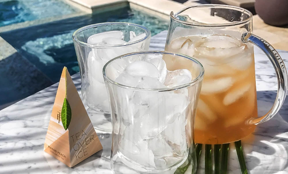 Tea Over Ice Pitcher set with green mango peach pyramid infuser by a pool with Poom glasses filled with ice