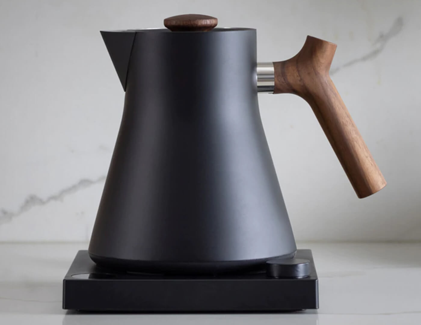 Black Corvo Kettle EKG with Walnut handle side view, resting on base, on kitchen counter