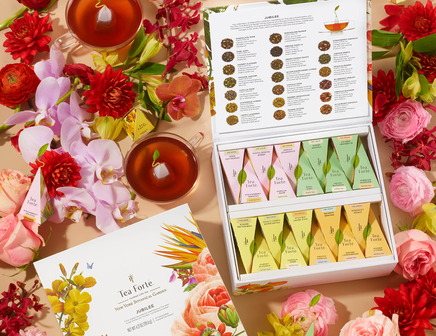 Jubilee Tea Chest of 40 pyramid tea infusers on table among flowers and teacups, open and closed boxes