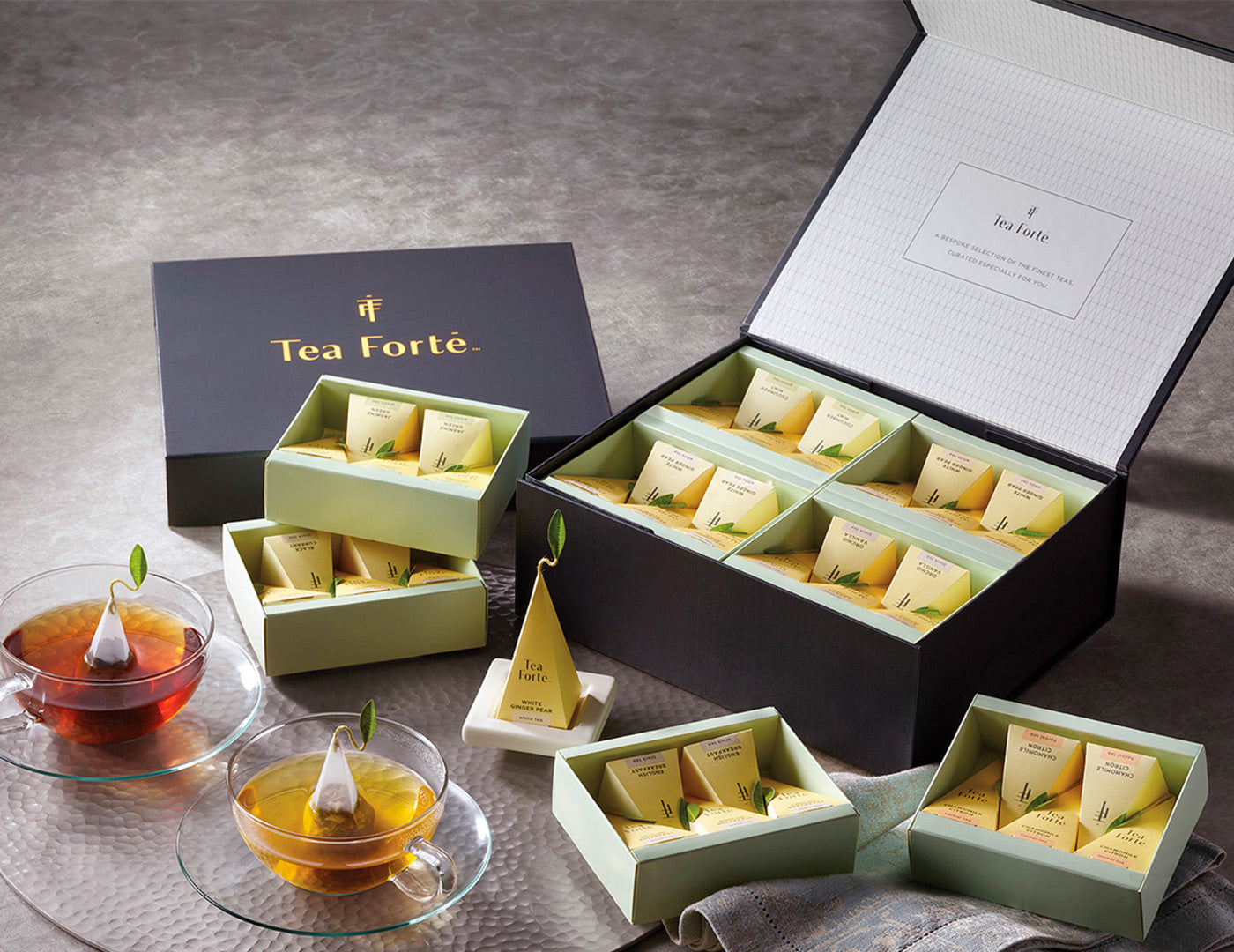 Tea Forté Select Chest of 40 pyramid tea infusers, open  on a table with glass teacups
