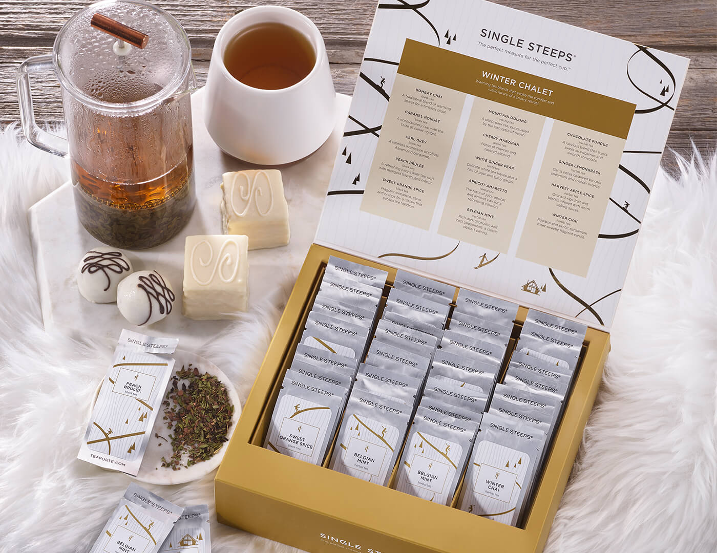 Winter Chalet Single Steeps® Tea Chest on a holiday table with teacup and French Press and open tea pouches.